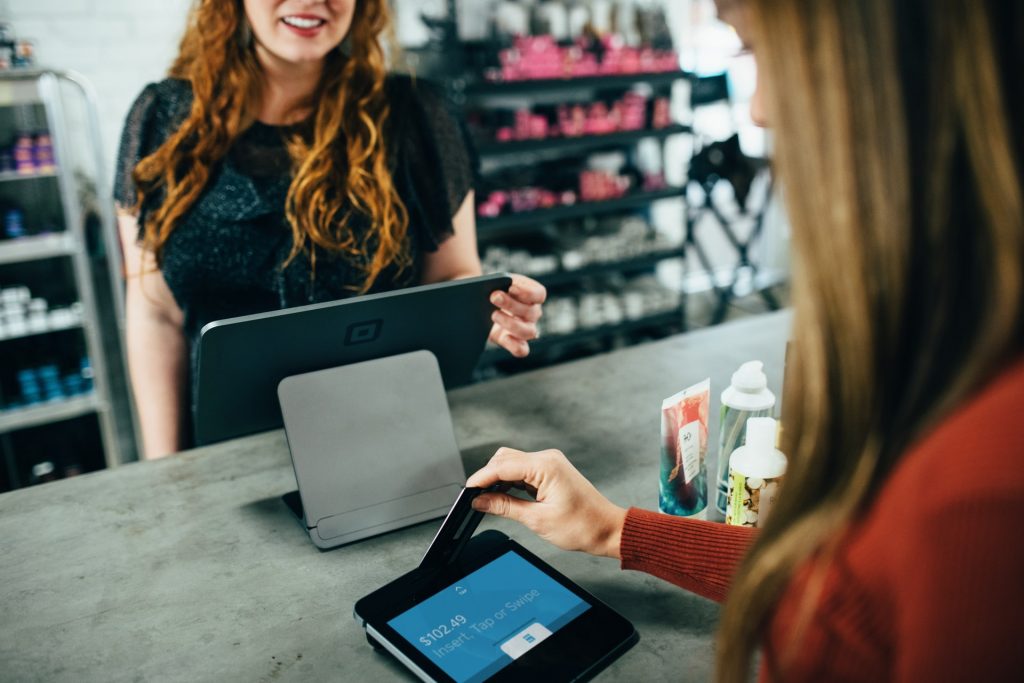 Photo of a woman behind a register and another woman using her credit card at a small business. 