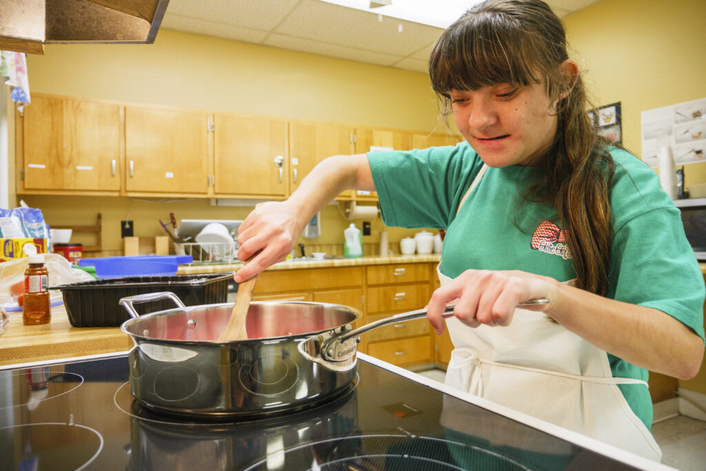 Student cooking in a kitchen stirring something in a pot. 