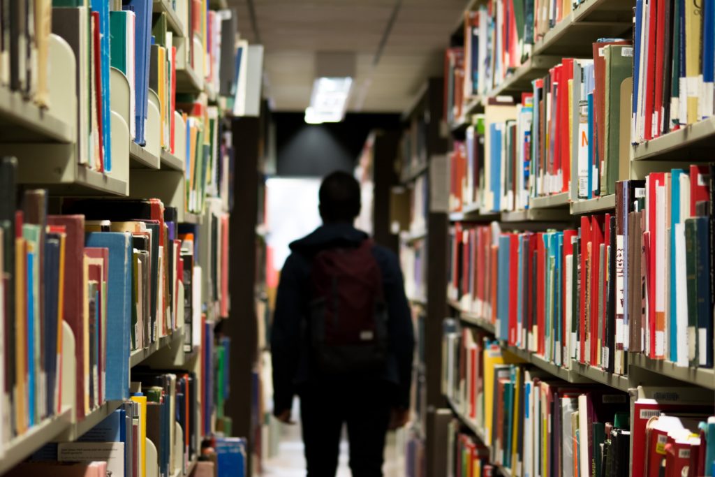 Person wearing backpack surrounded by books on shelves